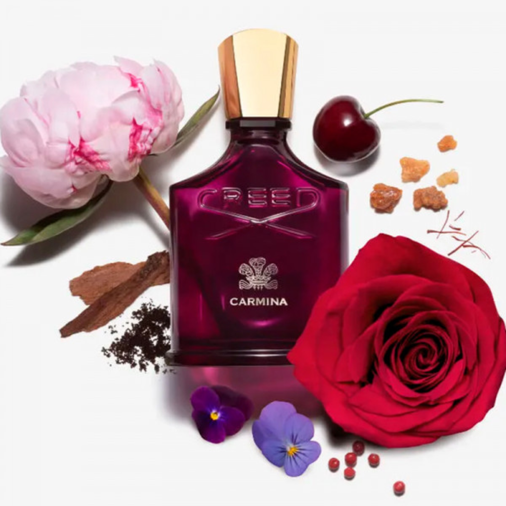 Artistic flat lay of Creed Carmina Eau de Parfum 75 ml bottle with rose petals and floral elements, showcasing the fragrance’s sensual blend of peony, violet, and myrrh.