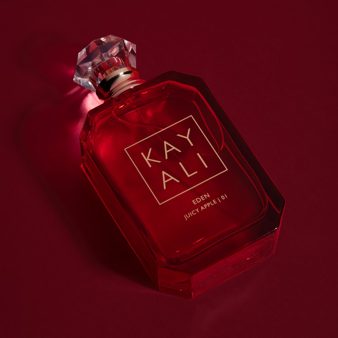 Kayali Eden Juicy Apple 01 EDP 100 ml perfume bottle showcased on a red backdrop, highlighting its rich, glossy design. A youthful fruity-floral perfume with notes of apple, wild berries, rose, and sugared moss — a joyful scent for spring and summer. Shop Fragrance Emporium.