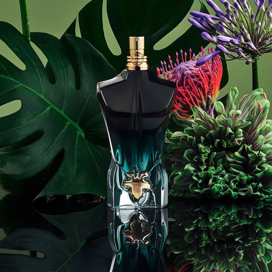 Jean Paul Gaultier Le Beau Le Parfum Eau de Parfum bottle placed in a lush tropical setting with exotic plants, representing the sensual paradise inspiration of this fragrance.